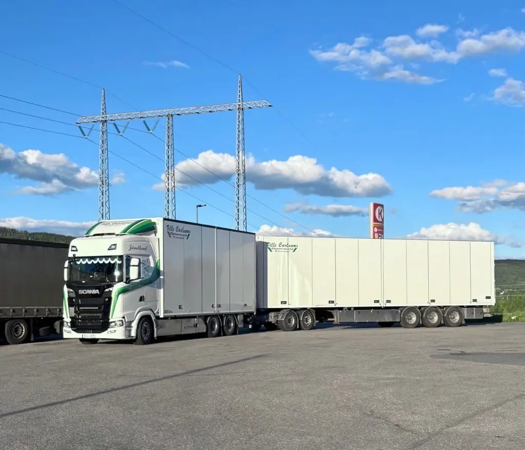 Vit Scania lastbil med släp, märkt med Ville Carlssons Åkeri, uppställd på asfaltsplan under blå himmel