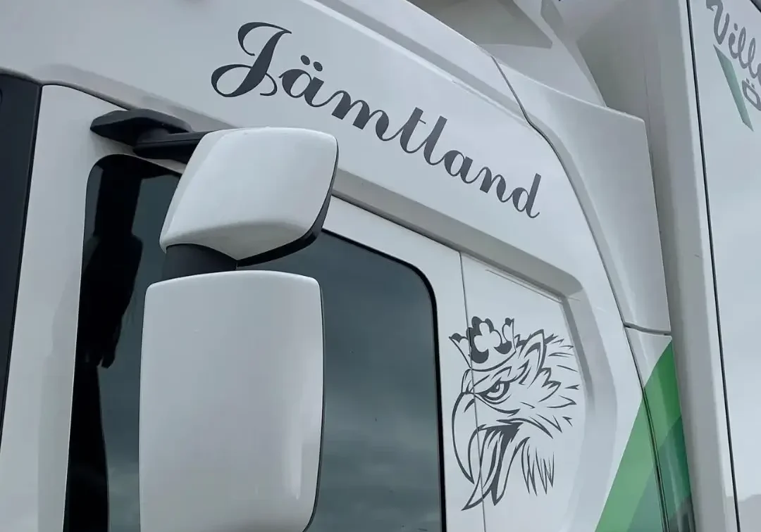 Närbild på Ville Carlssons Åkeris lastbil med texten 'Jämtland', örnlogotyp och sloganen 'Vi levererar!' i grönt.