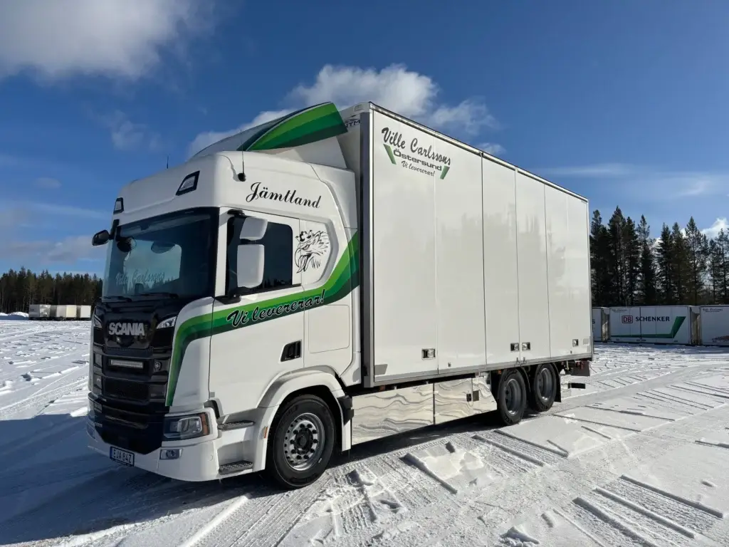 Vit lastbil från Ville Carlssons Åkeri parkerad på en åkeriterminal under vintern.